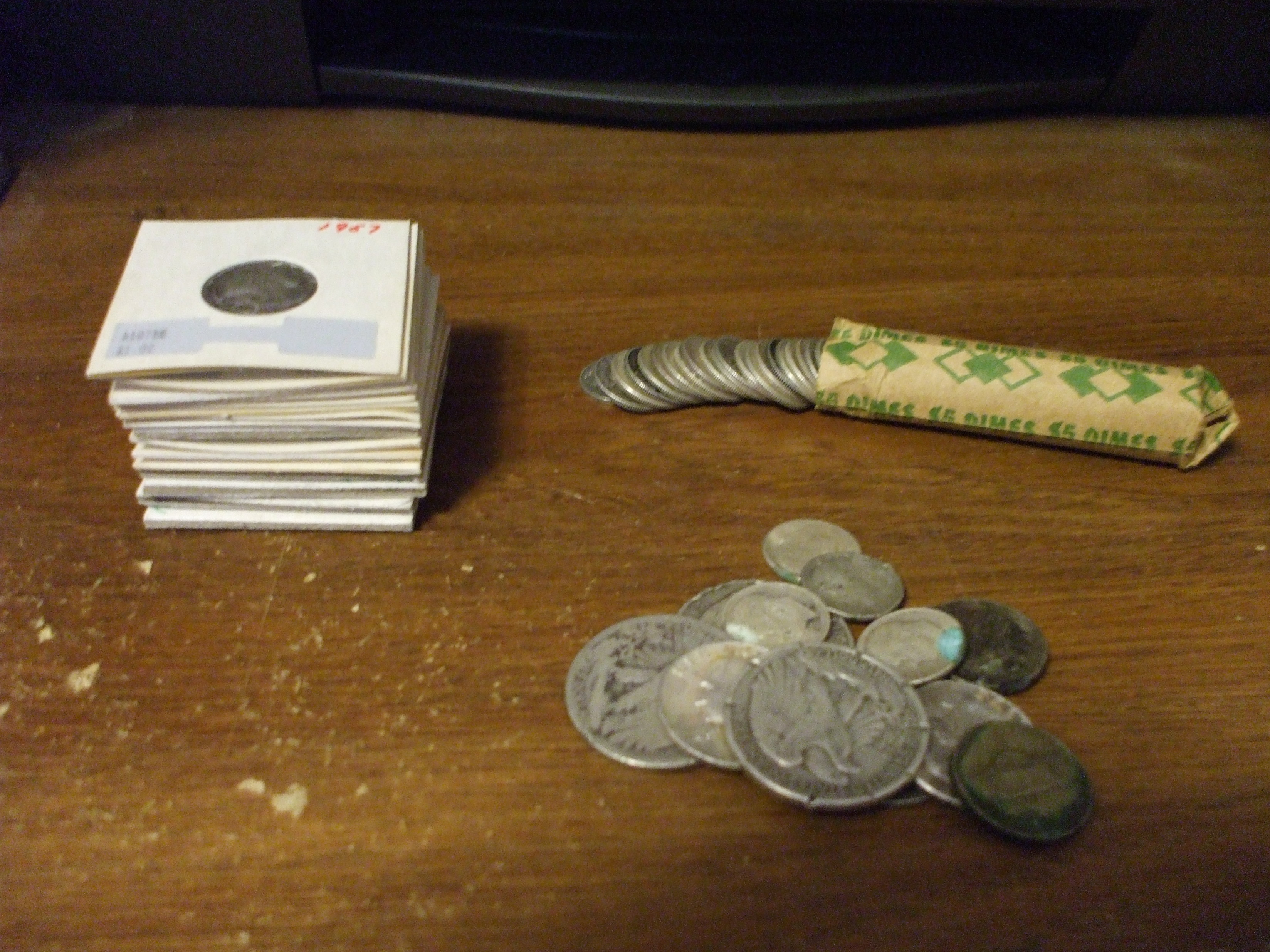 Silver dimes in paper coin holders alongside a mixed loose lot of half dollars, quarters, and war nickels