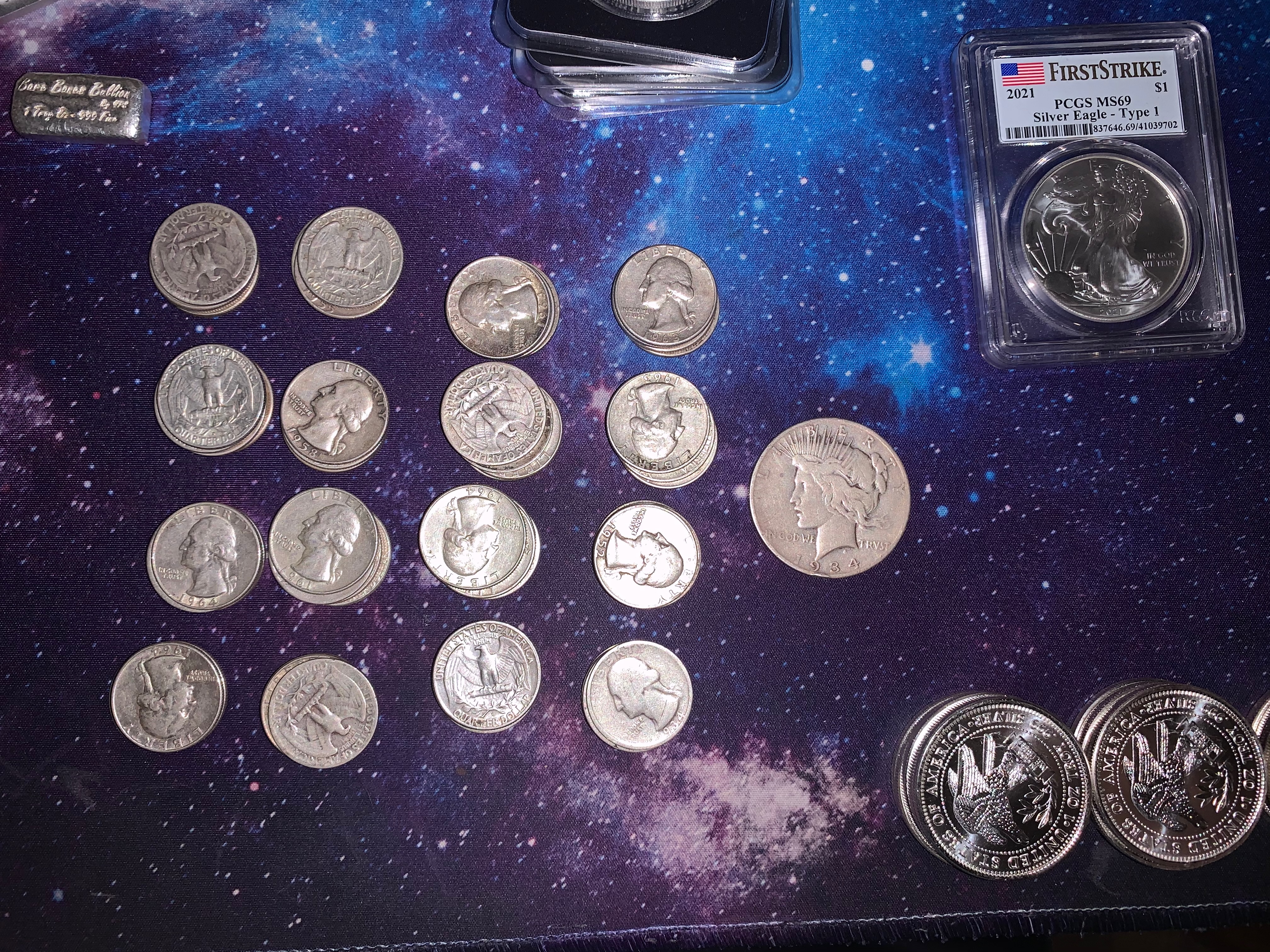 Washington quarters, Peace dollar, PCGS First Strike Silver Eagle, and silver rounds on a galaxy mat