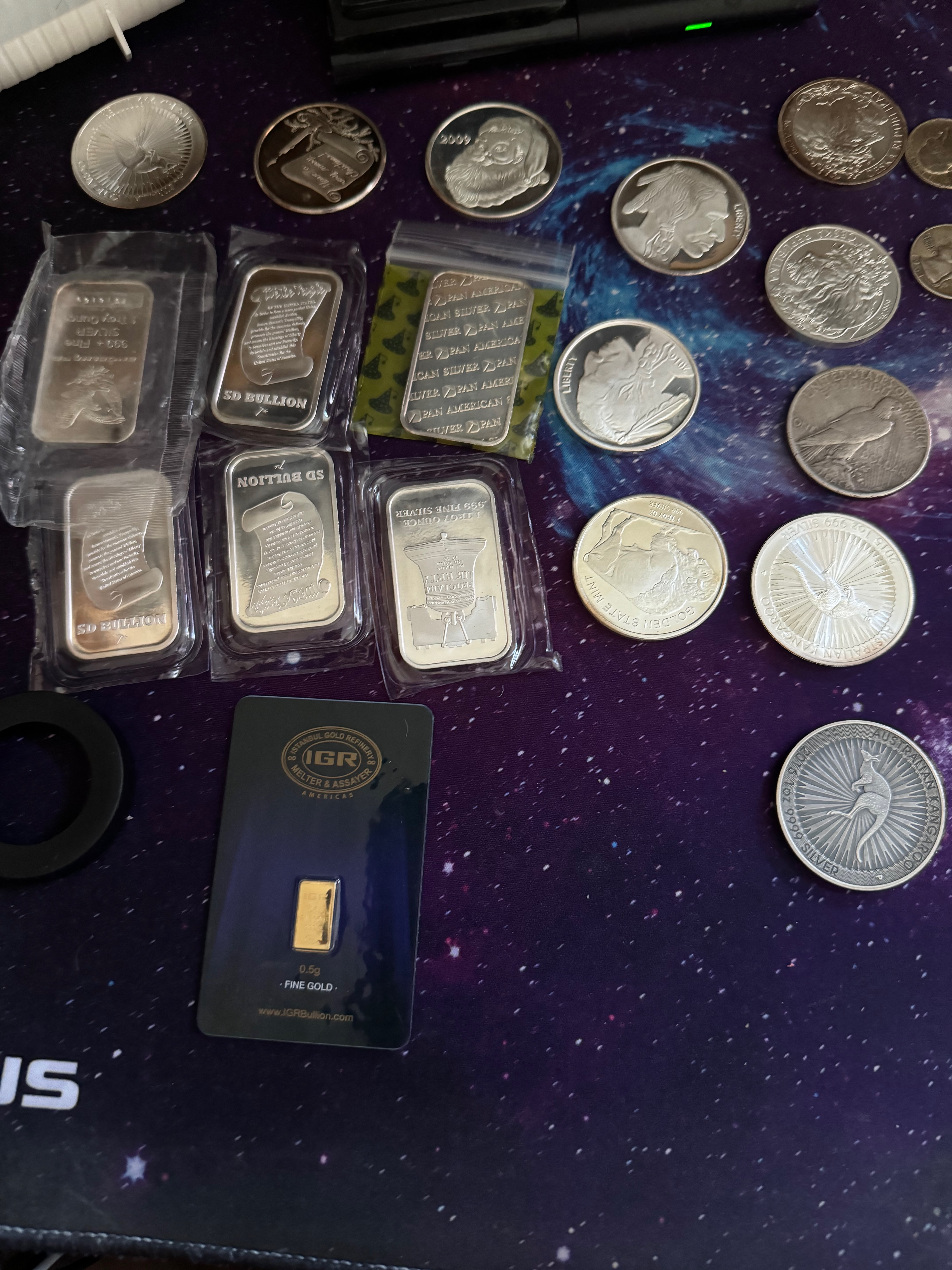 Silver bars in plastic sleeves, silver rounds, and a small gold bar on a dark mat
