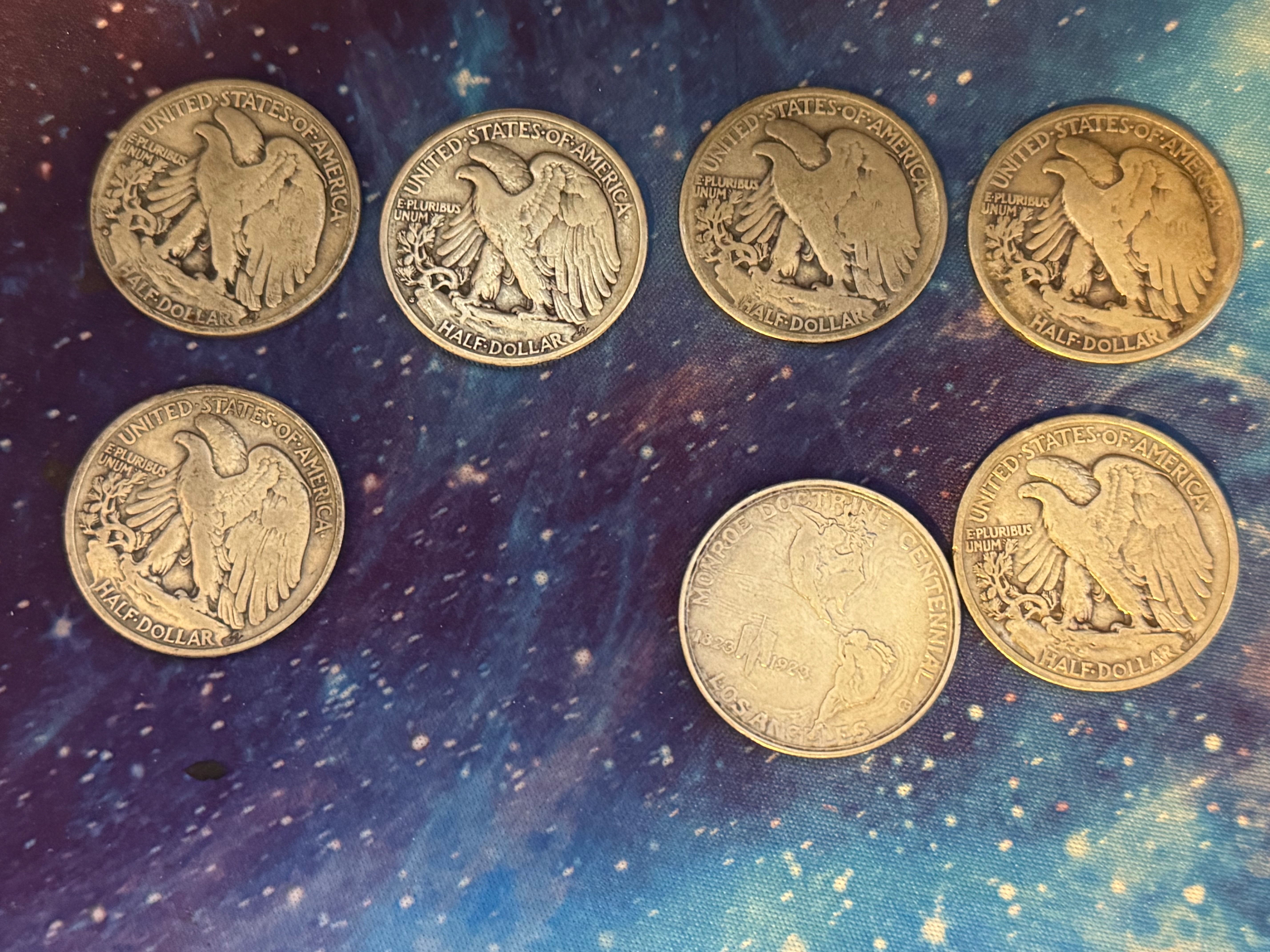 Seven Walking Liberty half dollar coins showing reverses on a galaxy desk mat